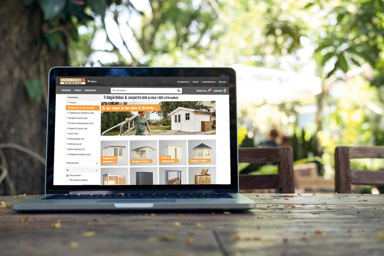 Laptop med Hornbachs webbutiksvy utomhus, fokus på trädgårdshus och carportar.