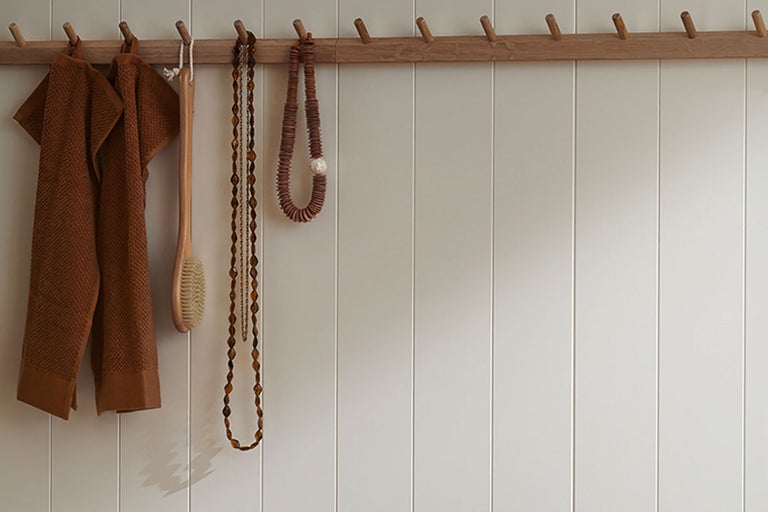Handdukar, borste och halsband på en klädhängare av trä framför en vägg med paneler
