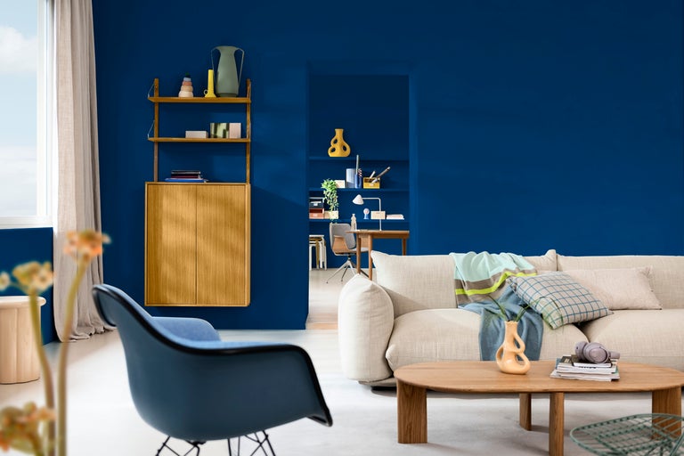 Vardagsrum med soffa, bord och hyllsystem mot en blå vägg