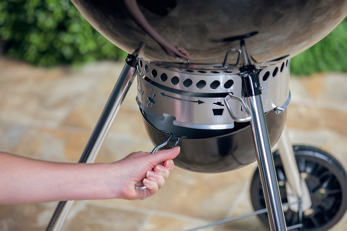 Kolgrill med hand som tömmer askbehållaren