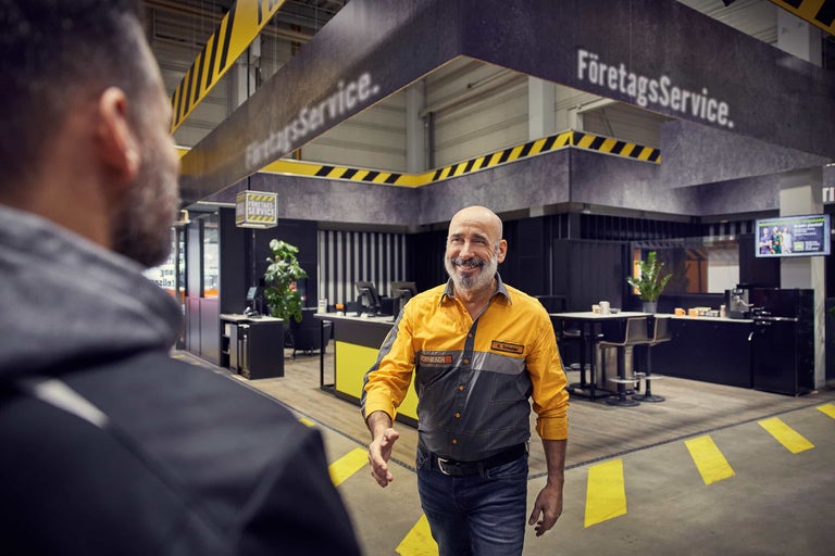 Hornbach-medarbetare i gulgrå arbetskläder välkomnar en kund i Företagsservice-området i ett byggvaruhus.