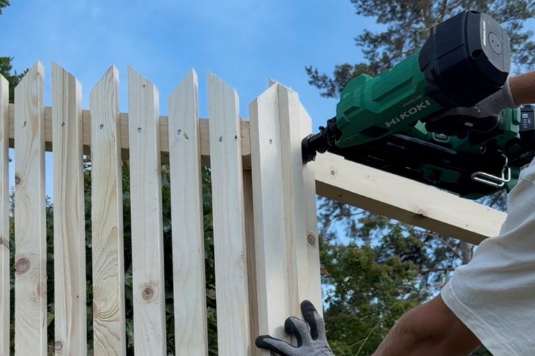 Batteridriven spikpistol från HiKOKI används för att fästa träspjälor på ett staket utomhus.