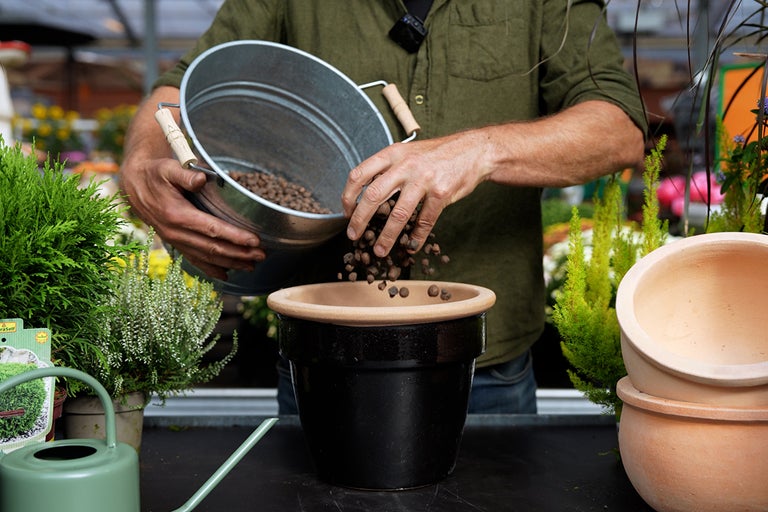 En person fyller jord från en metallhink i en blomkruka.