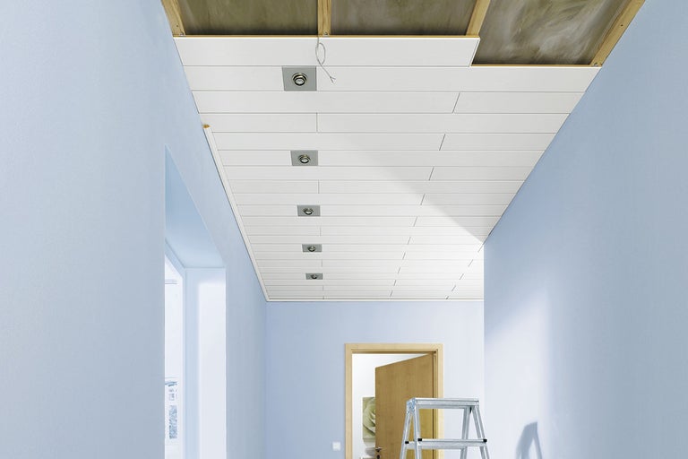 Tak med paneler, infällda spotlights och stege i en hall.