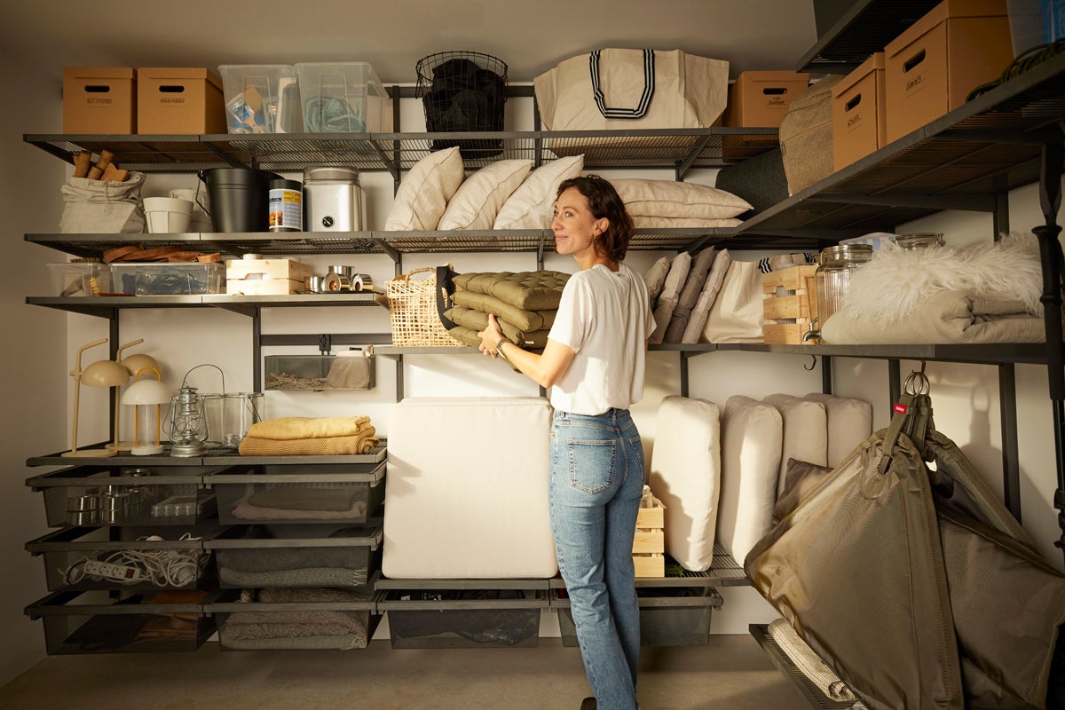 Kvinna förvarar kuddar i ett hyllsystem med olika förvaringsmöjligheter