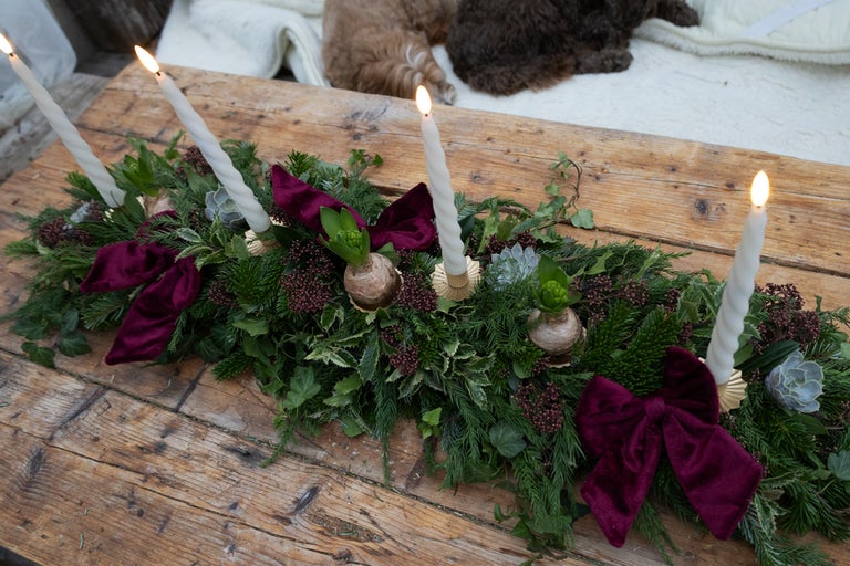 Dekoration med ljus, grangrönt och rosetter på ett träbord