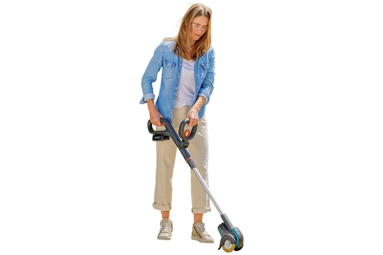 Kvinna använder en sladdlös fogborste i trädgården.