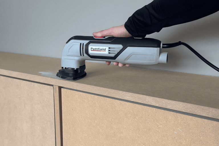 En person använder ett Pattfield multiverktyg för att slipa ett träskåp.