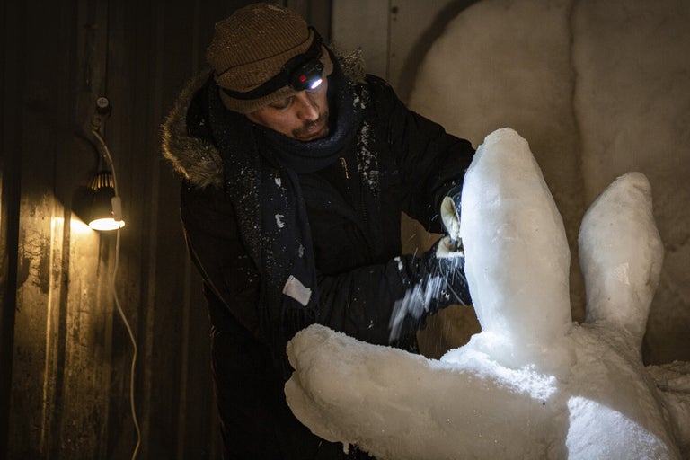 En man formar en skulptur av is med ett verktyg, upplyst av en pannlampa.