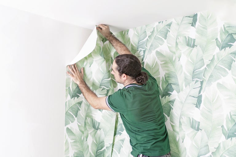Man fäster tapet med bananbladsmotiv på väggen