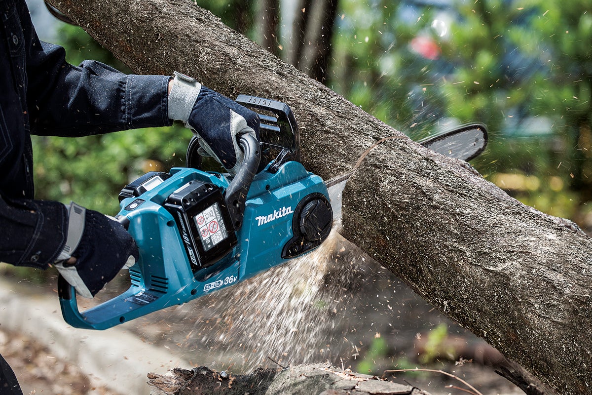 En Makita batteridriven motorsåg används för att såga en trädstam.