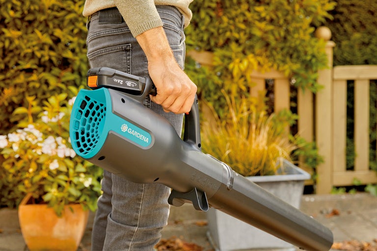 Man håller en Gardena sladdlös lövblåsare i trädgården.