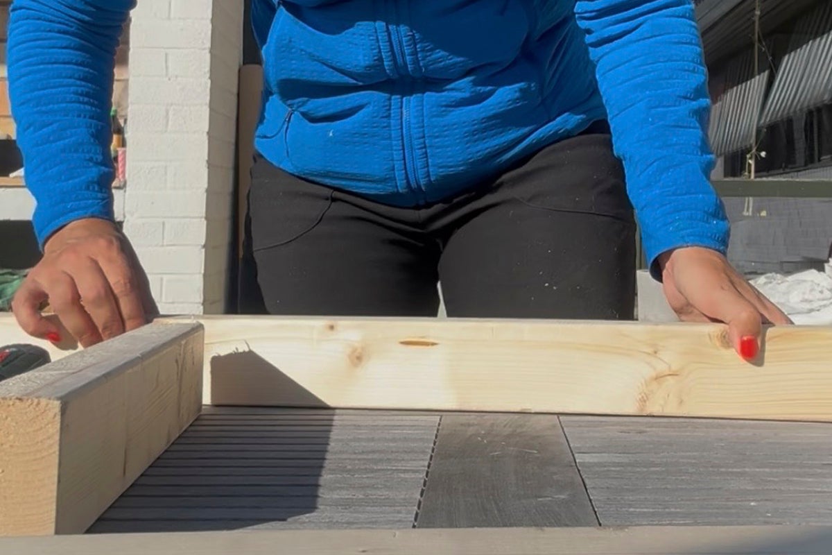 Person positionerar en obehandlad regel av gran på ett bord för hemmafix utomhus.
