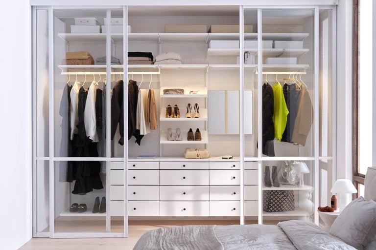 Öppen garderob med kläder, skor och lådor i ett ljust sovrum