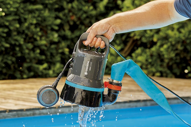 En Gardena dränkbar pump för klart vatten hålls ovanför en pool.