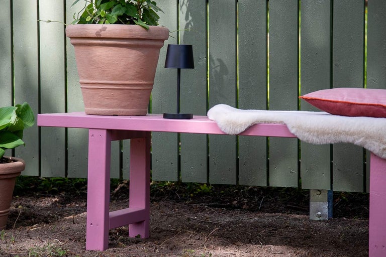 Trädgårdsbänk med blomkruka, bordslampa, kudde och fårskinn framför trästaket