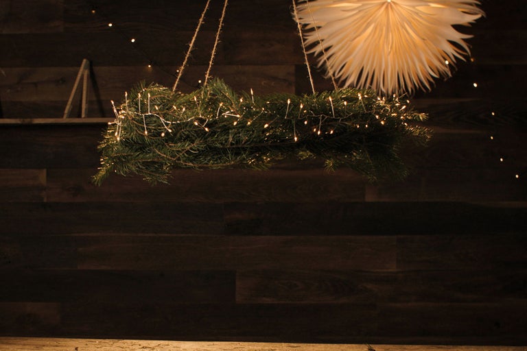 Hängande adventskrans med belysning och pappersstjärna framför trävägg