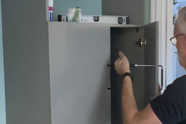 En man monterar ett grått skåp med en skruvmejsel.