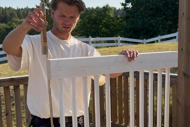 En man mäter ett vitt träräcke med en tumstock utomhus.