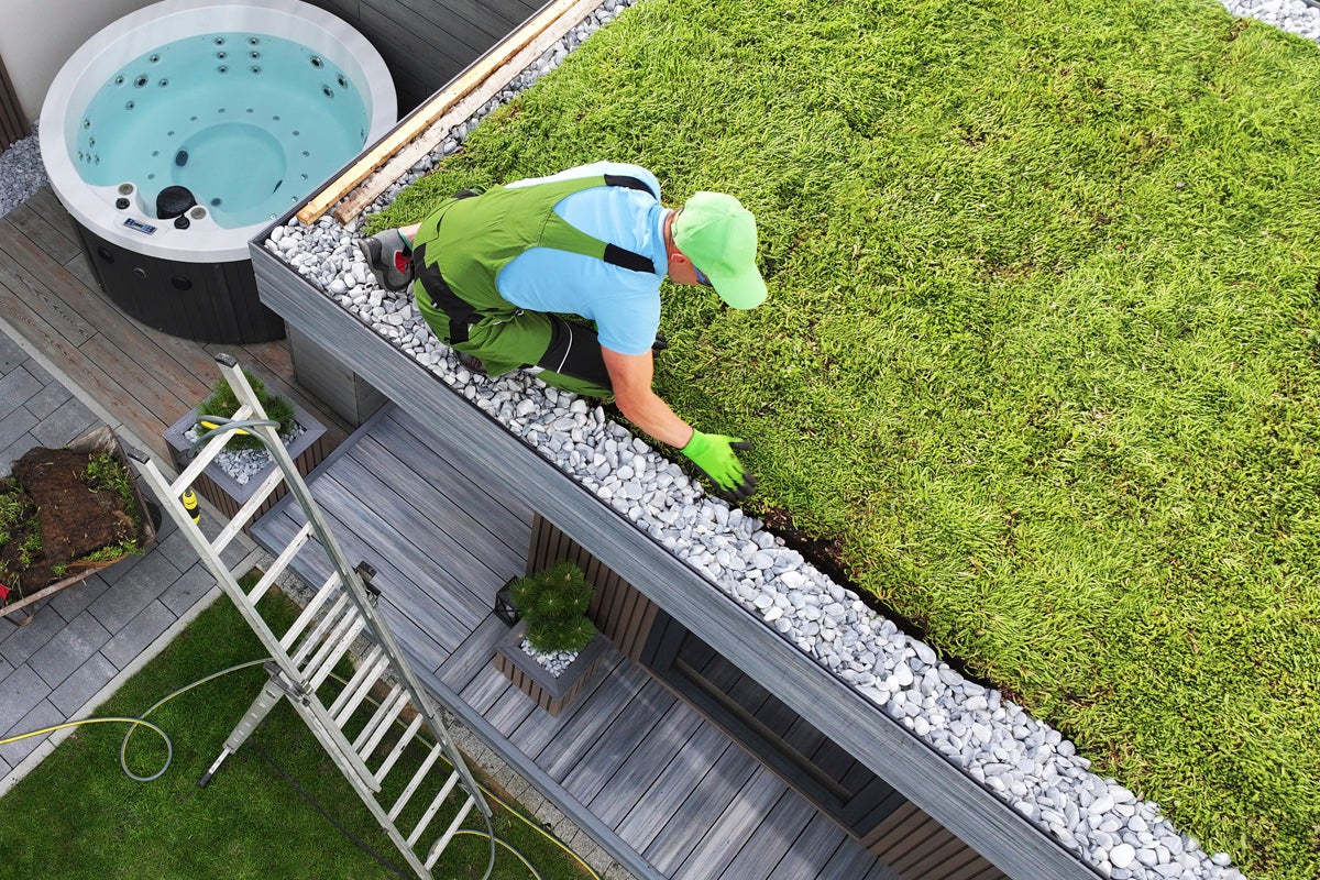 Man arbetar på ett grönt tak med en gruskant bredvid en bubbelpool