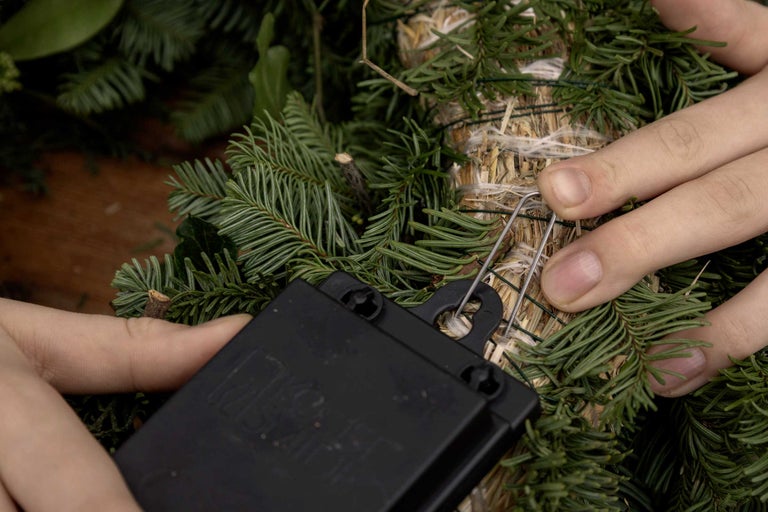 Närbild av en person som dekorerar en grangirlang med ett fästverktyg.