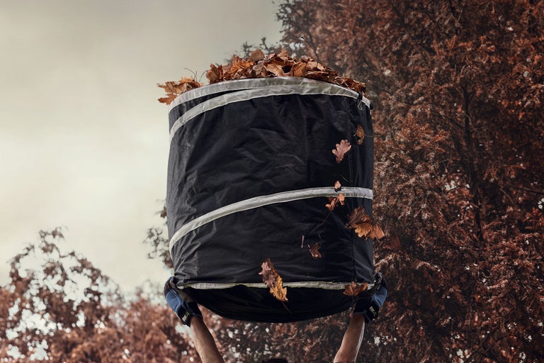 Trädgårdssäck fylld med löv hålls upp av person.