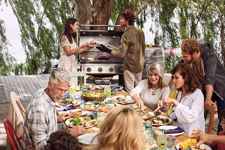 En grupp människor njuter av en måltid utomhus med en grill i bakgrunden.