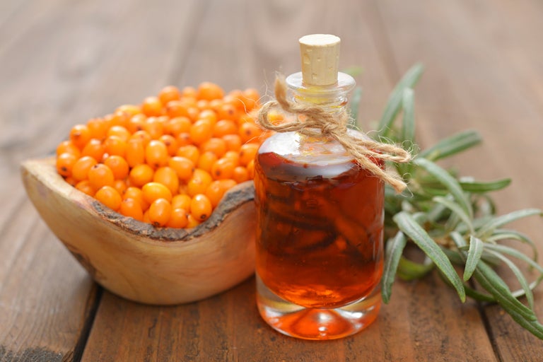 Havtornsolja i glasflaska och havtornsbär i träskål