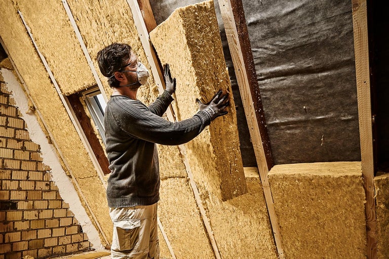 En man installerar värmeisolering på en vind, medan han bär skyddskläder.