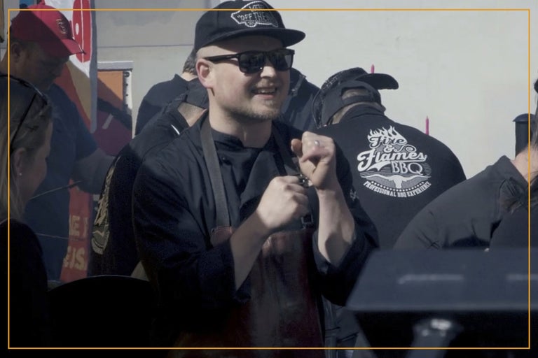 En man med ett förkläde omgiven av människor som grillar