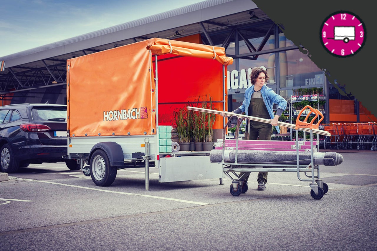 Scen med bilsläp, lastat med växter och byggmaterial, framför en Hornbach-butik.