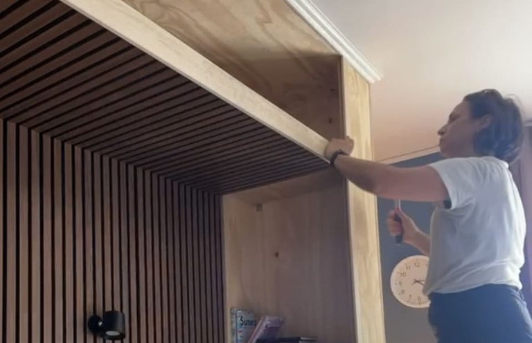 En person installerar dekorativ träpanel med ribbor som vägg och takbeklädnad i en modern interiör.