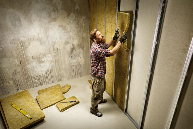 En man monterar mineralull för väggisolering i ett rum.