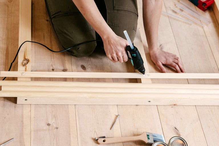 Person använder limpistol på träribbor