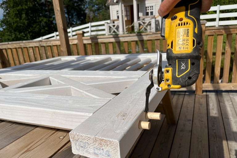 Oscillerande multiverktyg med DeWalt Logo kapar träpluggar på ett vitmålat trästaket på en altan.