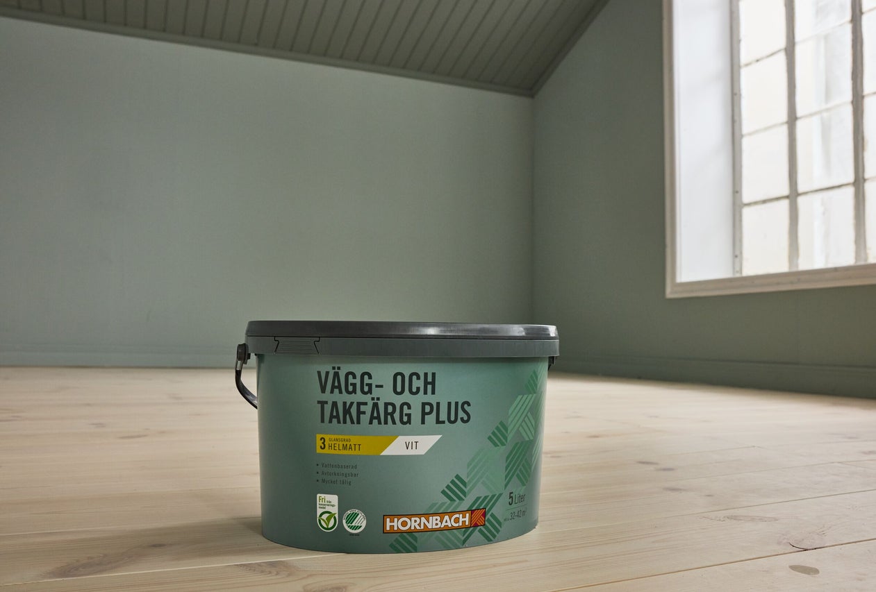 En 5-liters hink Hornbach Vägg- och Takfärg Plus i vitt, helmatt, på ett trägolv i ett ljust och tomt rum.