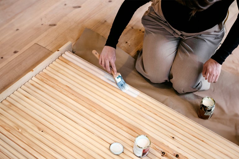 En person målar träpinnar med en borste, där färg och borste är synliga.