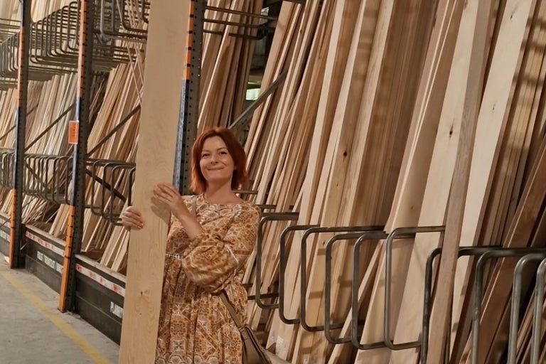 Kvinna håller en träplanka i en trähylla på Hornbach