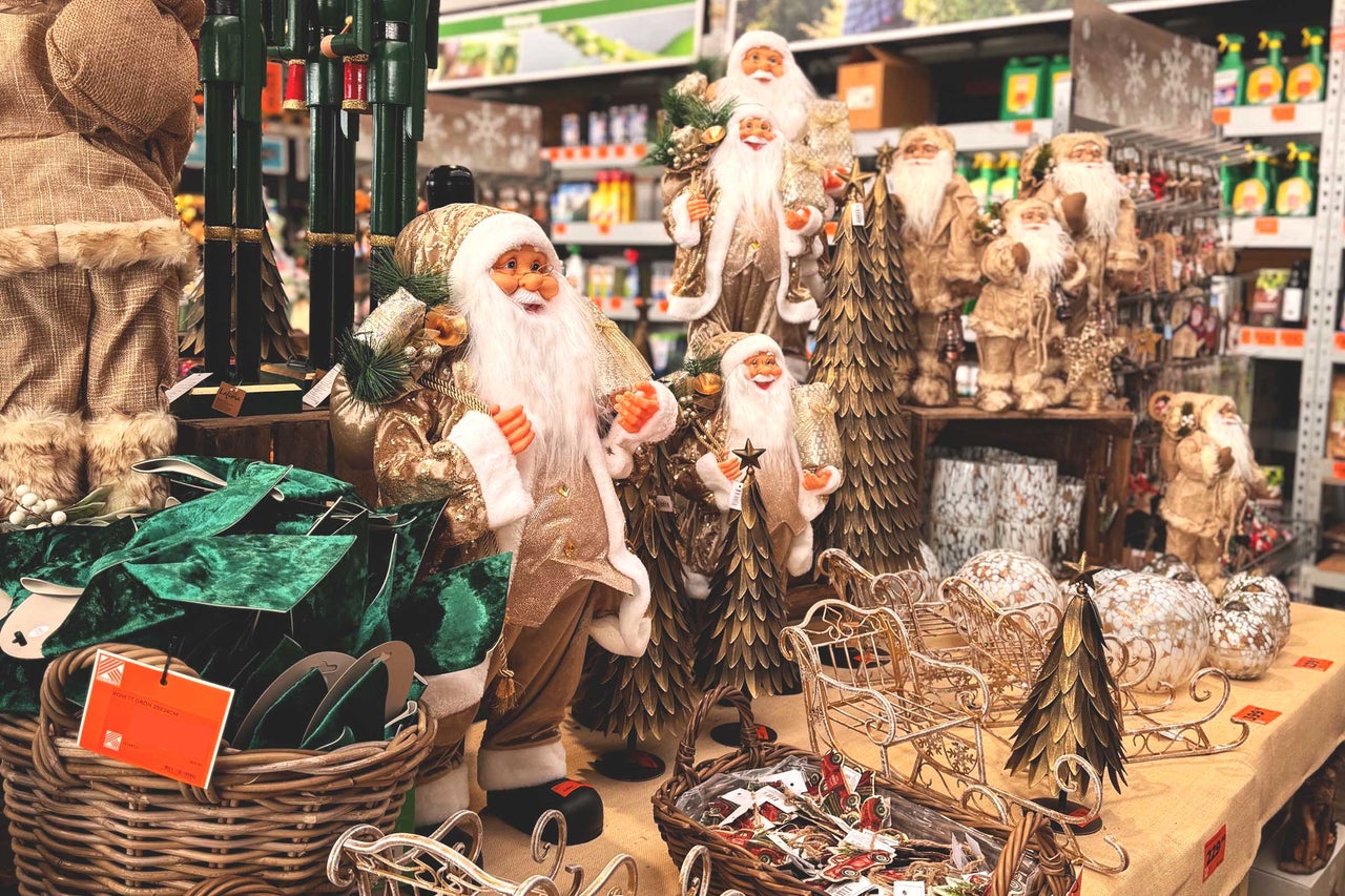 Dekorativ julscen med jultomtefigurer, julgranar och slädar på ett bord i en butik.