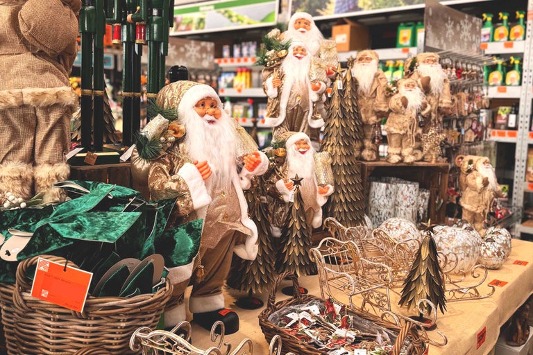 Dekorativ julscen med jultomtefigurer, julgranar och slädar på ett bord i en butik.