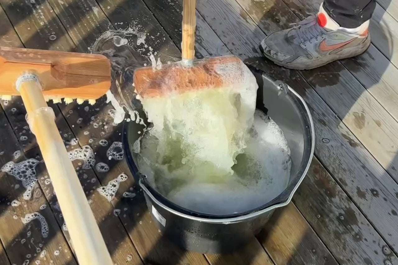 Träborste doppas i en hink med såpvatten för rengöring av en träaltan.