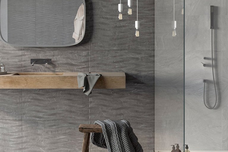 Modernt badrum med gråa väggplattor, tvättställ och dusch.