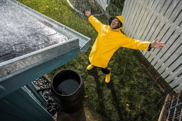 Man i regnkläder är glad över att en regntunna fylls under ett takrännsystem i regnigt väder.