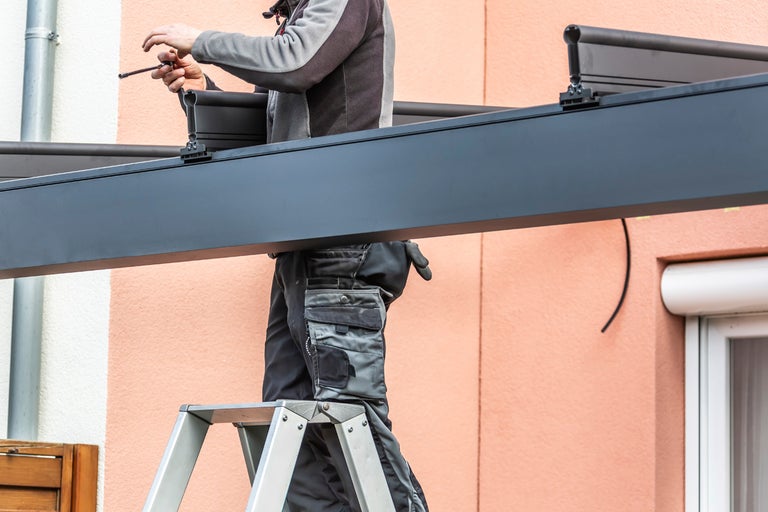 En montör på en stege monterar ett terrasstak.