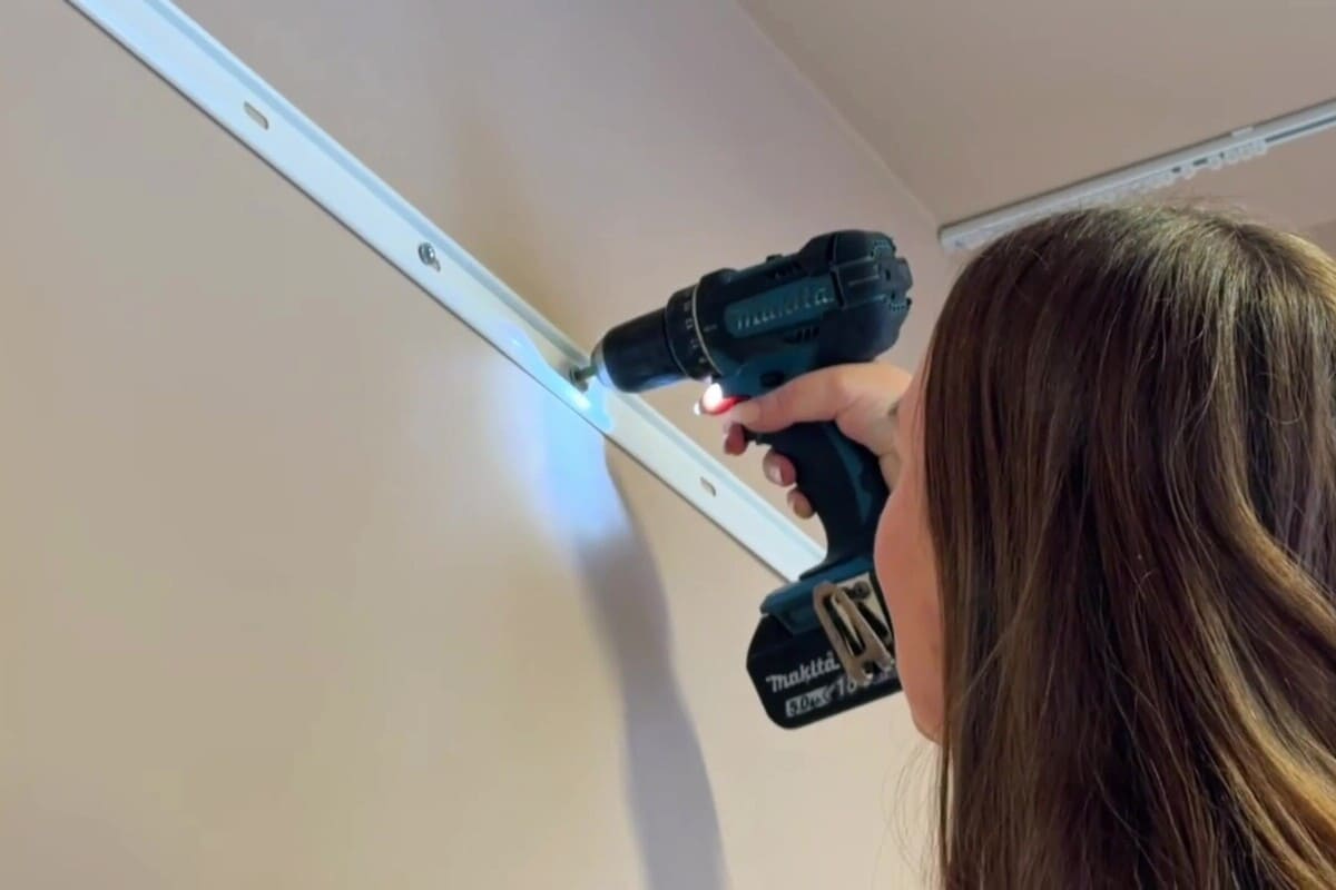 En kvinna fäster en gardinstång på väggen med en batteridriven skruvdragare.