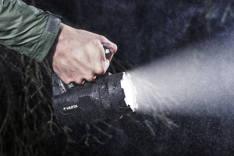 En person håller en Varta handlampa i regnet.