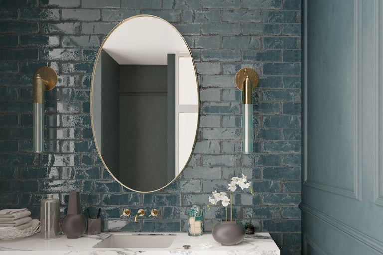 Modernt badrum med oval spegel, vägglampor och glänsande kakel