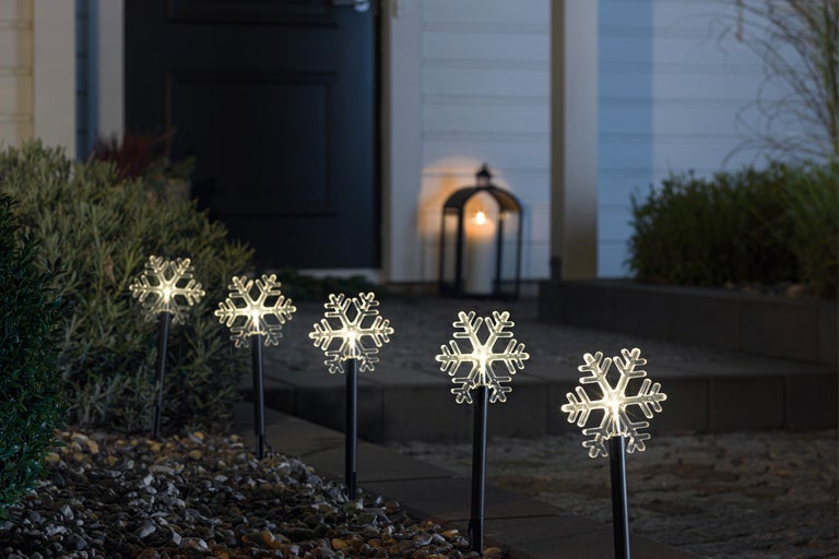 Dekorativa snöflingor trädgårdspluggar lyser upp en trädgård.