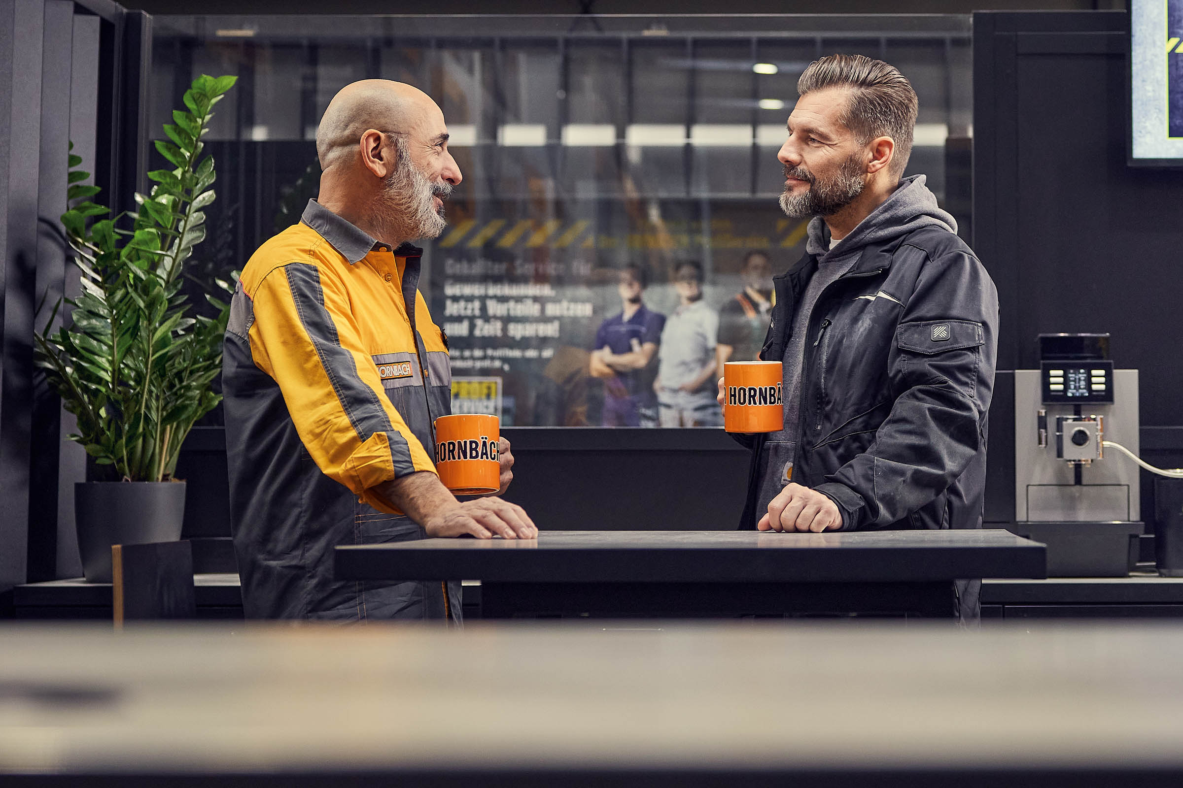 Två män står vid ett bord och håller i Hornbach-muggar.