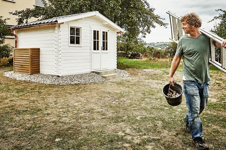 Trädgård med redskapsbod, träpanel och en man med en stege och hink
